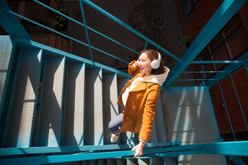 a woman in a yellow coat with headphones walks around the city.  copy space. 