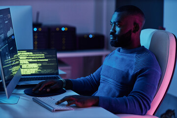 Portrait of software engineer writing code at workplace in neon lights