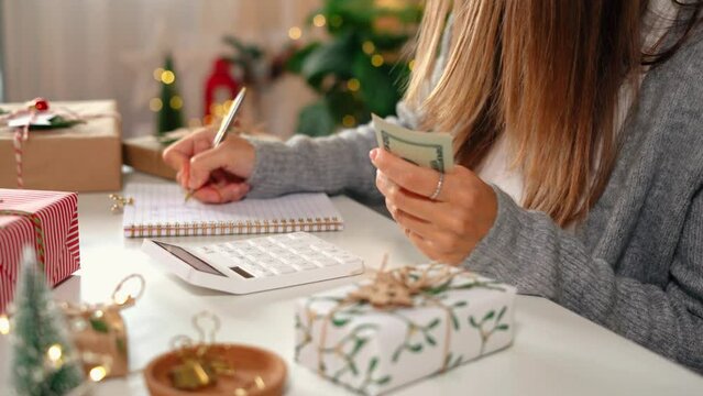 Girl counting US Dollar bills, using calculator, and writing expenses. Woman doing budget, estimating money balance for shopping spree. Female accountant paying taxes. Girl counting Christmas gifts.