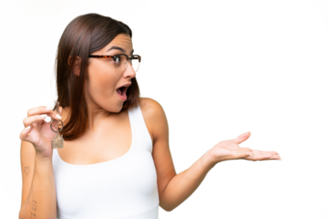 Young caucasian woman holding home keys isolated on green chroma background with surprise facial expression