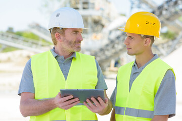 two workers on a construction site using a tablet