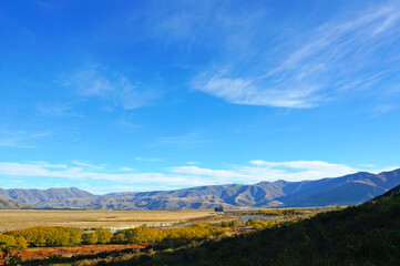 Scenic blue shaded mountain range and dry farmland under bright blue autumn sky.