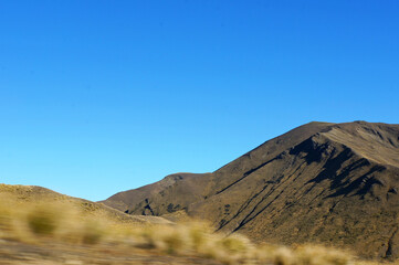 Scenic blue shaded mountain range and dry farmland under bright blue autumn sky in scenic Mackenzie District, South Canterbury, New Zealand