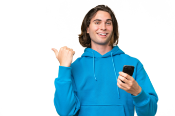 Young handsome man isolated on green chroma background using mobile phone and pointing to the lateral