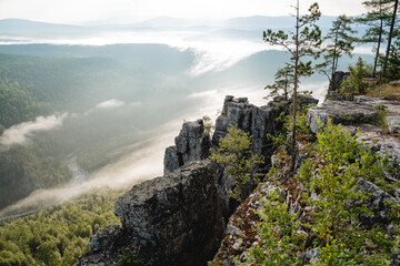Naklejka premium The dawn of the day in the mountains, the morning fog creeps in at the bottom of the river valley, the smoke rises from the bottom up into the mountains, a rock cliff.