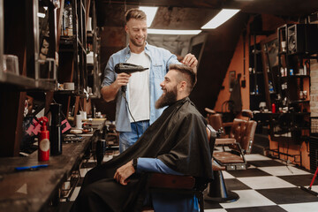 Young adult hairdresser at the barber shop with a client smiling
