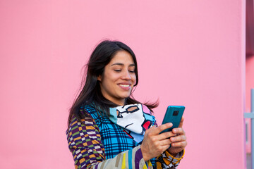 Woman with colorful t-shirt on pink background sending a message with the phone