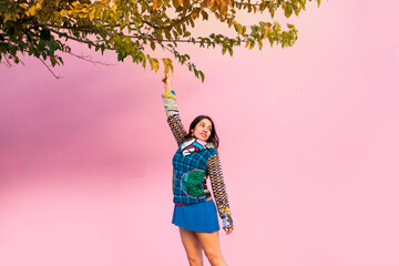 latin woman with colorful dress taking leaves from a tree on a pink background