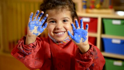 Kids, school and education with happy children having fun and painting with hands in kindergarten. Female child hand painting on paper. Portrait of little girl smiling at camera at preschool - Powered by Adobe