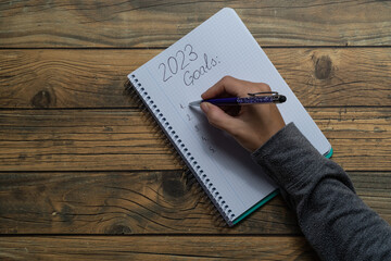 Close-up of a young woman's hand writing in a notebook her New Year's resolutions for 2023.
