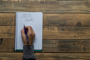 Close-up of a young woman's hand writing in a notebook the New Year's resolutions for 2023 with...