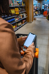 person with a shopping cart holding a phone with a white screen in a supermarket