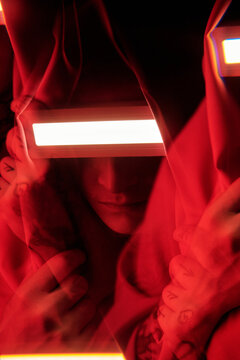 Close-up of young man hiding his face behind luminous glasses covering with mantle