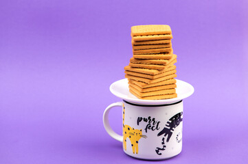 Cookies and cup of coffee. Stacks of tasty cookies on the white plate. Square biscuits on the violet background with copy space. Healthy eating..