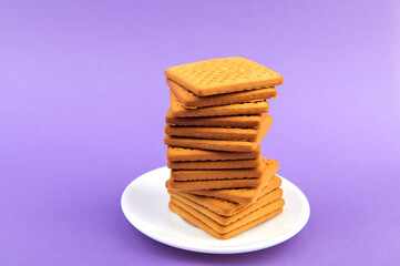 Stack of square biscuits on white plate isolated on purple violet background