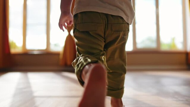 baby runs to mom at home. a child with bare legs runs across the floor to his mother against a sunny window. happy family kid dream concept. kid running back view lifestyle at home hugging mom
