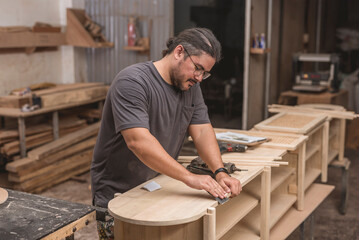A man sandpapers the edges of a newly built shoe bench at his furniture workshop.