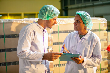 Asian workers with clipboard is checking product bottles of fruit juice on the production line in the beverage factory. Manufacturer checks quality of food industry.