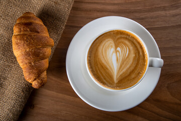 croissant with in white cappuccino on wooden table