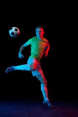 Fototapeta na wymiar Dynamic shot of young active football player in action isolated on dark background in neon light. Concept of sport, goals, competition, achievements.