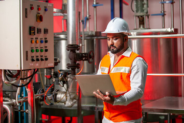 Professional engineers with helmets work to maintain industrial construction equipment, workers are inspecting or repairing machines  with laptop.