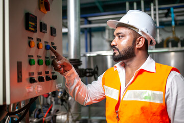 Asian engineer worker wearing safety uniform control operating  machine and turn on switch in industry factory.