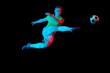 Fototapeta na wymiar Sport in action. One man professional soccer player training with football ball isolated on dark background in neon light filter. Sport, speed, power and energy