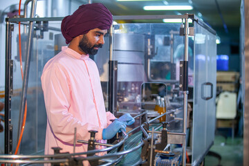 Asian man worker with clipboard is checking product bottles of fruit juice on the production line in the beverage factory. Manufacturer checks quality of food industry.