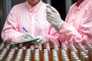 Asian woman worker with clipboard is checking product bottles of fruit juice on the production line in the beverage factory. Manufacturer checks quality of food industry.