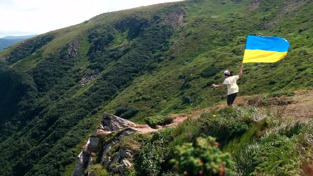 young happy woman holding ukrainian flag on the cliff of carpathian mountains