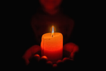 Little boy holding red burning candle in the darkness.Selective focus.Closeup.