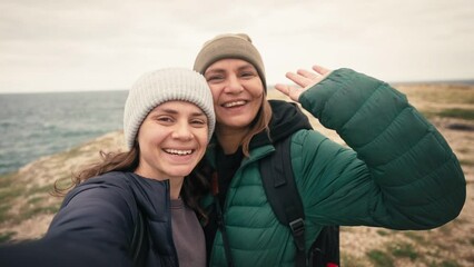 Slow-motion footage of a happy lesbian couple taking a selfie while traveling to the winter sea. - Powered by Adobe