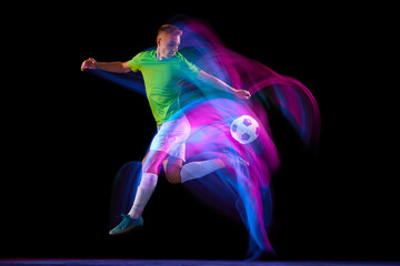 Dribbling. Young soccer, football player in motion and action with ball isolated on dark background...