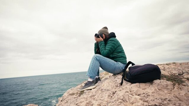 Slow-motion footage of a woman photographer taking pictures of the seascape with a camera while traveling.