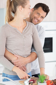 young married couple embraces standing near table in kitchen