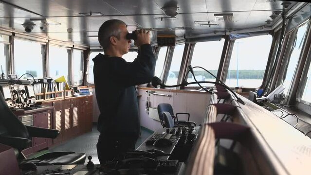 Deck officer with binoculars on navigational bridge. Seaman on board of vessel. Commercial shipping. 