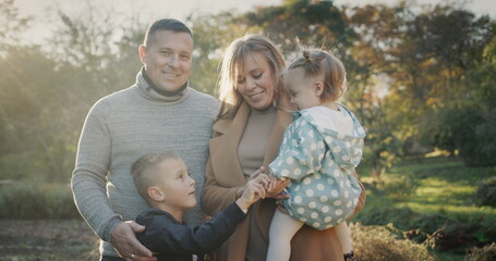 Portrait of a young healthy family - a couple with two children. Smiling, looking at the camera. Standing in the autumn park