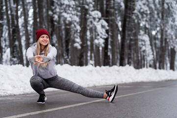 Beautiful young sport woman doing stretching fitness exercise in winter forest