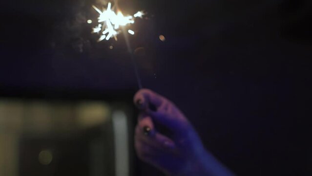 Woman with burning sparkler moves her hand in circle in dark at home. Christmas and New Year. Family holiday and fun. Bengal fire in slow motion