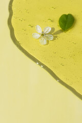 Transparent cosmetic gel or serum of yellow color with a white flower and green leaves on a beige background. The concept of natural cosmetics. Top view. Selective focus.