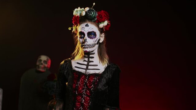 Beautiful lady of dead posing in halloween costume with skull make up to celebrate dios de los muertos on mexican holiday. Spooky woman as santa muerte with black and white body art. Handheld shot.