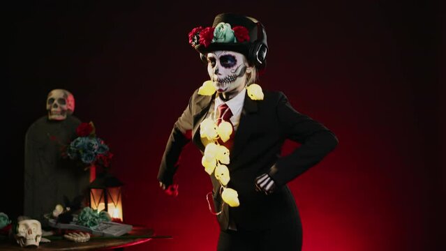 Scary woman with costume of death dancing in studio, listening to music on headphones and doing dance moves. Looking like holy mexican goddess to celebrate dios de los muertos. Handheld shot.