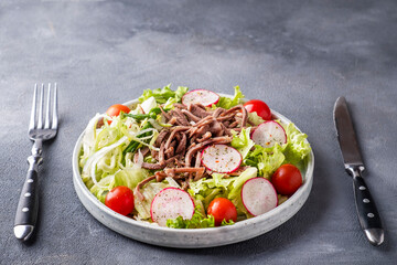 Salad with boiled beef tongue and vegetables on a plate served with fork and knife. Text space