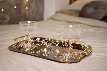 Beautiful glasses are on a tray, with bokeh lights in the background. There is a tray of glasses on the bed in the bedroom. Romantics