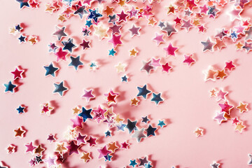 Multicolor holographic Stars Glitter Confetti on pink background. Festive backdrop, selective focus