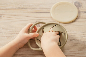 Unrecognizable child taking piece of food out from pastel gray silicone snack cup near lid at...