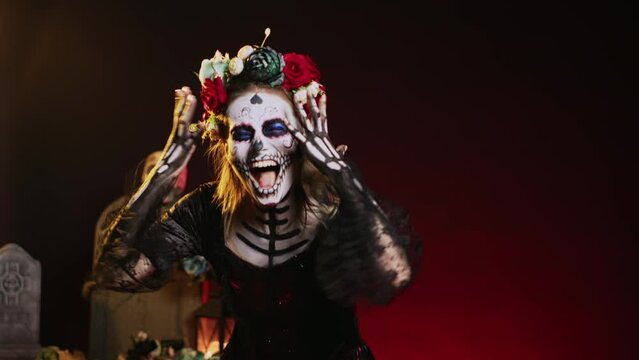 Horror lady of death screaming loud dressed in costume with skull body art, wearing flowers crown. Yelling like holy cavalera catrina, acting creepy to celebrate dios de los muertos. Handheld shot.