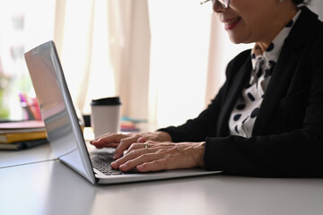 Smiling middle aged businesswoman working online on digital marketing project with laptop computer at her workstation