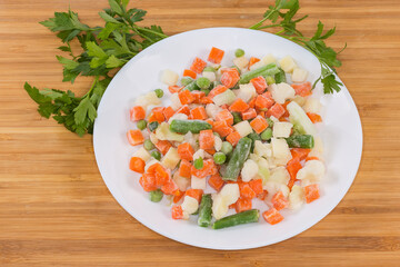 Different sliced frozen vegetables on dish on wooden surface