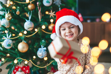 Laughing little girl with gift box near the Christmas tree